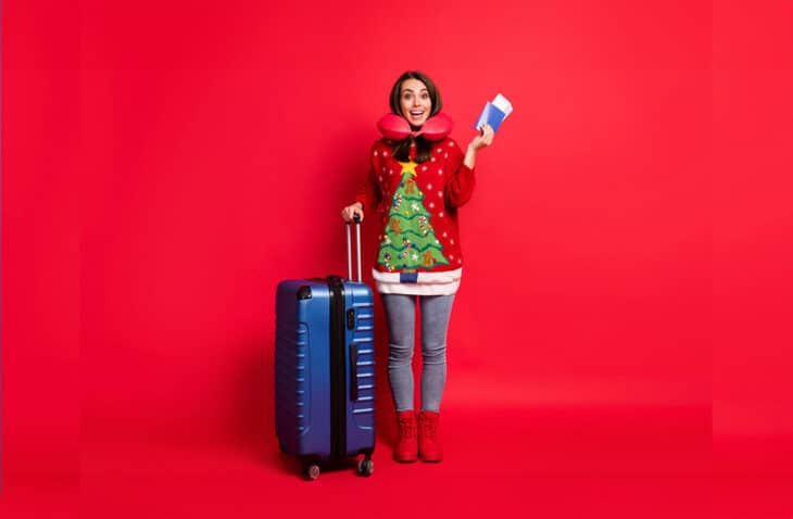 Woman in Christmas sweater holding her passport, boarding pass, and luggage