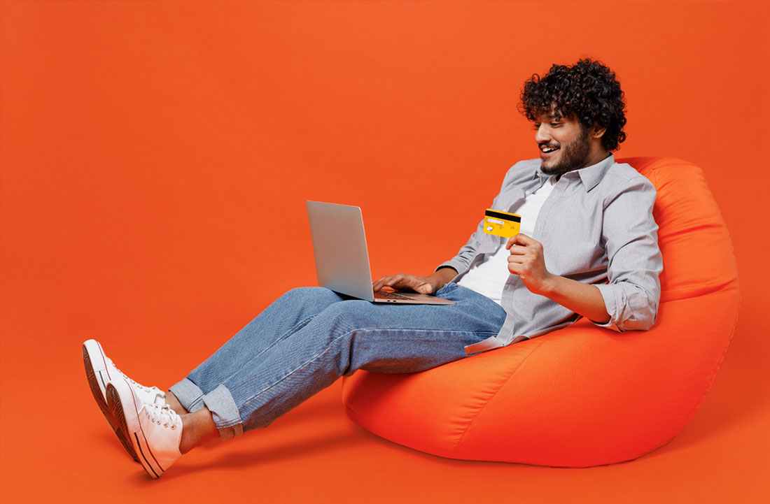 Man on a bean bag holding credit card and laptop