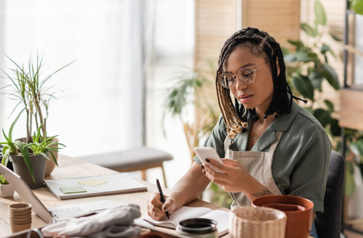 business owner looking at phone and writing on notepad