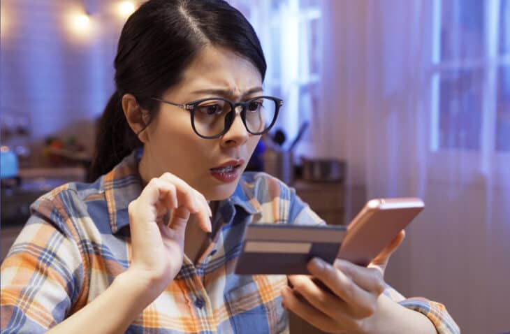 Mujer con mirada preocupada mirando su teléfono, sosteniendo su tarjeta