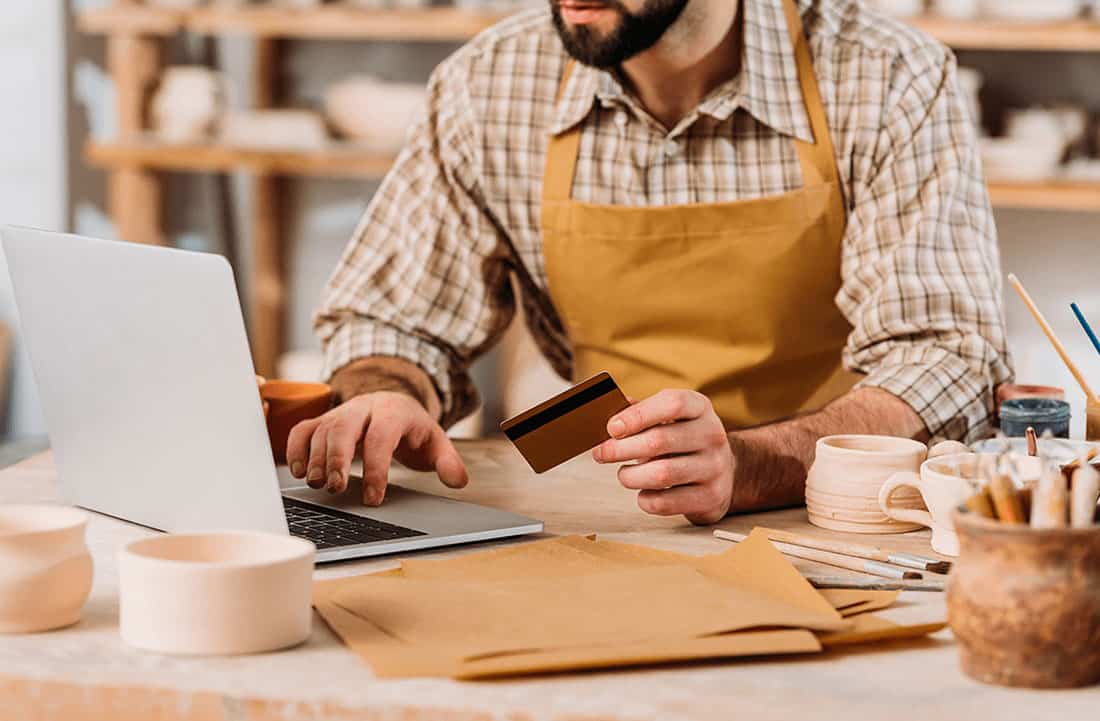 Dueño de un negocio de cerámica usando su tarjeta para realizar compras en línea