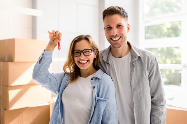 Man and woman holding keys in front of moving boxes.