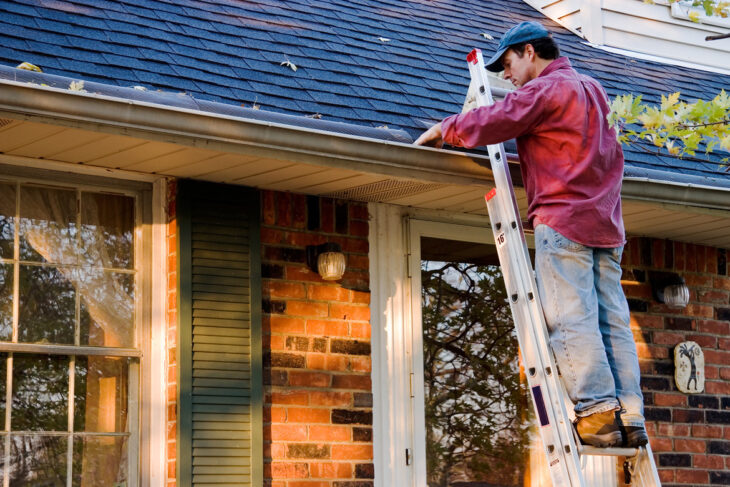 A man on a ladder working on the roof of a house.