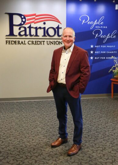 Ron standing in fornt of Patriot Logo