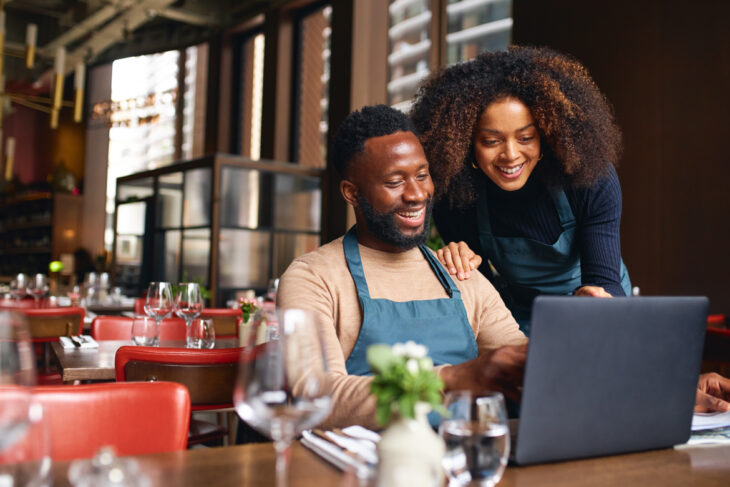 A man sitting and looking at the computer with a woman behind him.