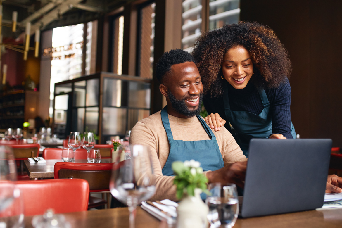 A man sitting and looking at the computer with a woman behind him.