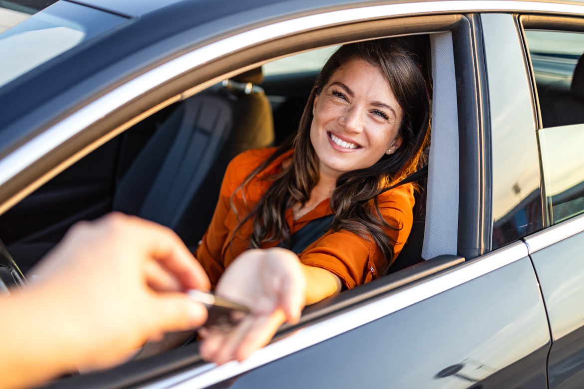 Woman being handed keys while sitting in her car.